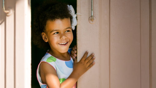 Smiling girl peeking while standing at doorway