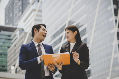 Low angle view of business people discussing file while standing against building in city