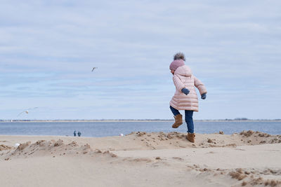 Cute girl fooling around at the beach in a winter coat