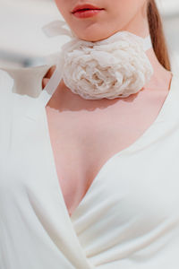 Elegant fashion details of white satin bridal dress and with a rose accessory around the neck.