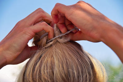 Close-up of blond woman tying hair with elastic against clear sky