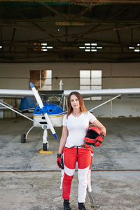 Young female skydiver in a plane hangar with a plane behind her