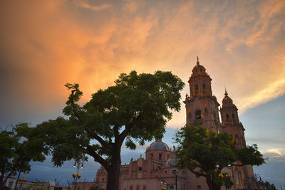 Low angle view of trees and building against sky during sunset