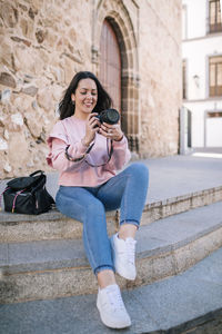 Full length of smiling young woman sitting outdoors