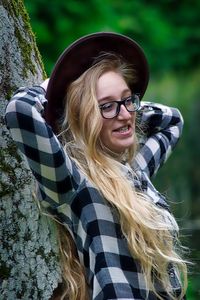 Smiling young woman looking away while leaning on tree