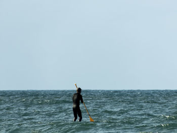 Rear view of man standing in sea against clear sky