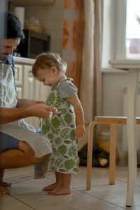 Father tying apron to baby boy in kitchen at home