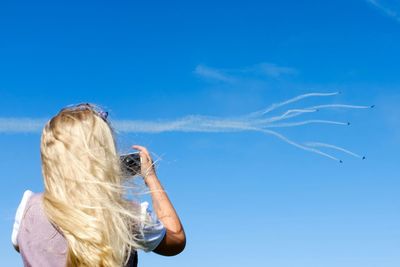 Low angle view of woman standing against blue sky