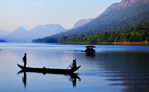 People in boat sailing on lake against sky