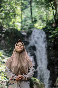 Smiling woman standing against waterfall