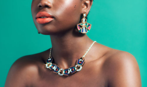 Close-up of young black woman against green blue background wearing statement jewellery