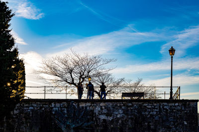 Silhouette bare trees by street against blue sky