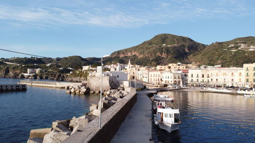 Sailboats moored on sea by buildings in city against sky