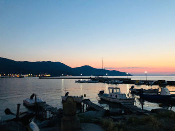 Boats moored in harbor at sunset