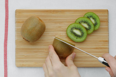 Directly above shot of woman cutting kiwi on cutting board