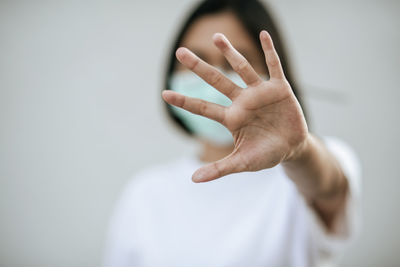 Close-up of woman wearing mask showing stop sign against wall