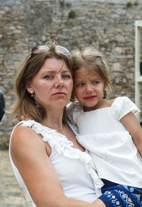 Portrait of mother carrying crying daughter against wall