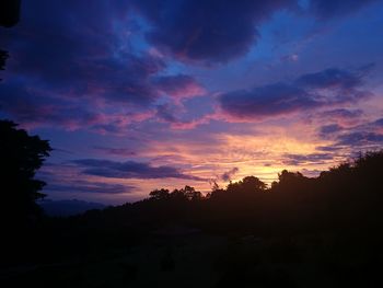 Silhouette trees against dramatic sky during sunset