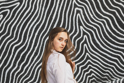 Portrait of young woman standing against graffiti wall