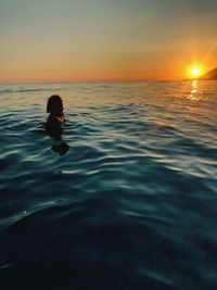 Woman swimming in sea against sky during sunset