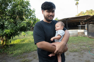 Father and son holding baby while sitting on plant
