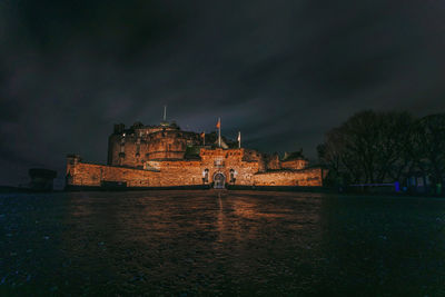 Illuminated buildings by river against sky at night