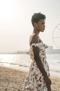 Side view of woman with short hair standing at beach against clear sky