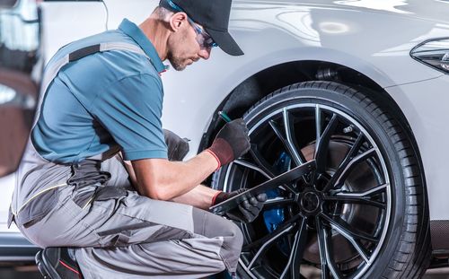 Side view of man examining car with checklist in garage