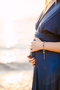 Side view of pregnant woman standing at sea shore against sky