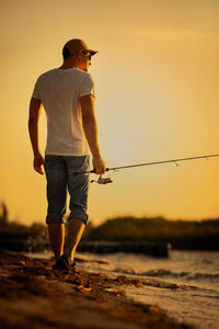 Full length of man standing on beach against sky during sunset