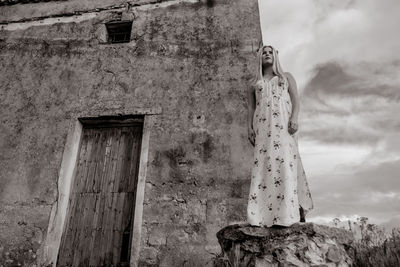 Low angle view of woman standing by old abandoned building against sky