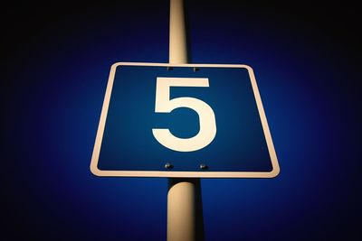 Low angle view of road sign against clear blue sky