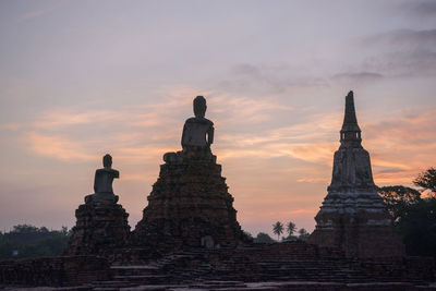 Low angle view of temple and buddha statues against sky during sunset