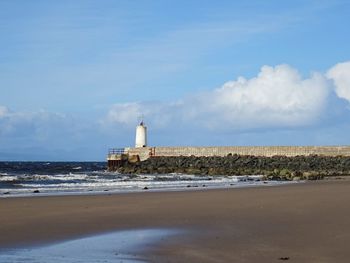 Lighthouse on beach by sea against sky