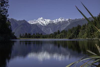 Scenic panoramic view of calm lake with reflection and snow capped mountains against sky