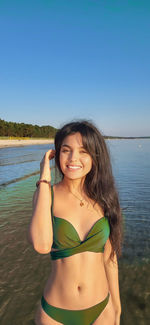 Young woman in bikini standing in sea against clear blue sky