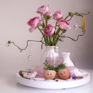 Pink roses in vase with easter eggs on plate against wall