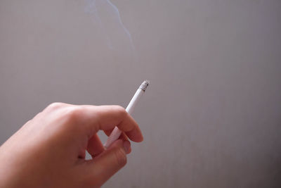 Cropped hand holding cigarette against wall