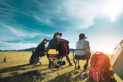 People sitting on field by land against sky