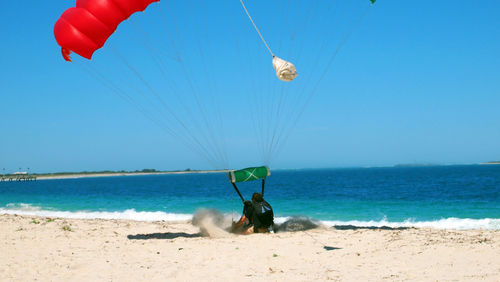 Man paragliding at beach against clear sky