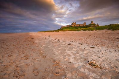 Bamburgh castle by beach against cloudy sky