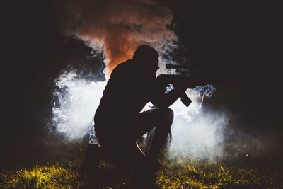 Silhouette man with weapon kneeling on field at night