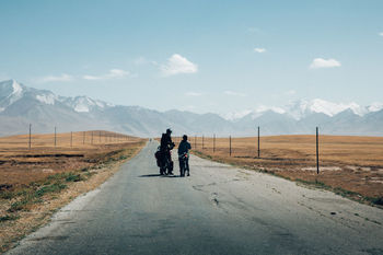 REAR VIEW OF PEOPLE RIDING ON ROAD