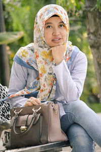 Portrait of young woman wearing hijab while sitting on bench