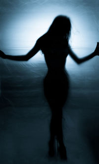 Rear view of silhouette woman standing against curtain