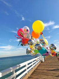 Multi colored balloons on beach against sky