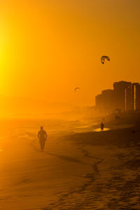 Silhouette man flying over beach against sky during sunset