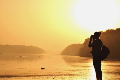 Silhouette man photographing at beach against clear sky during sunset