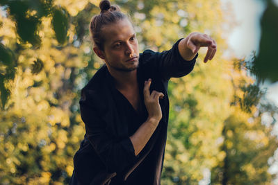 Thoughtful young man looking away while gesturing while standing against plants