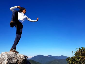 Low angle view of man standing on rock against clear sky